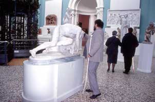 A visually impaired visitor is lead to a statue through the tactile paving